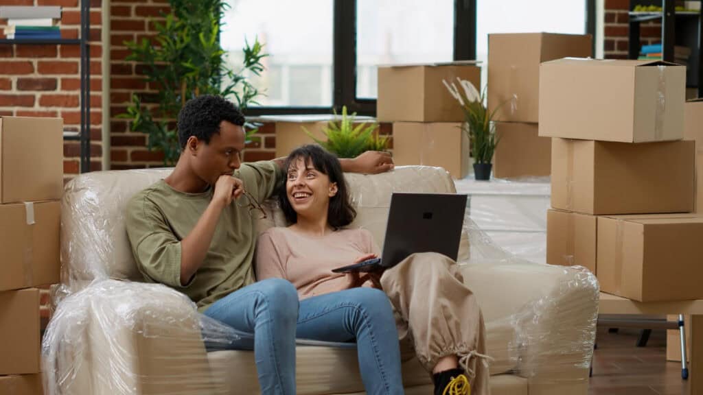 Couple smiling on couch among moving boxes.