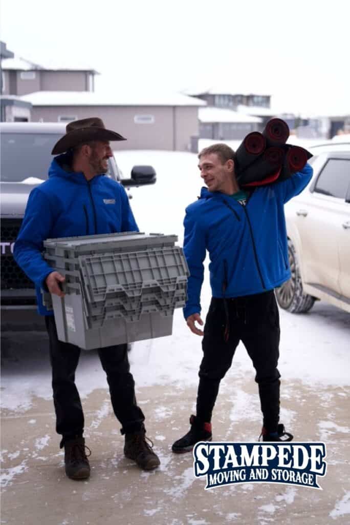 Two movers carrying boxes in snowy weather.