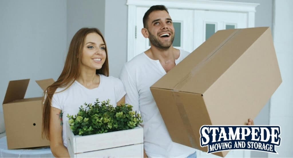Happy couple moving into a new home with boxes and plants highlighting a smooth stress-free relocation with Stampede Moving and Storage