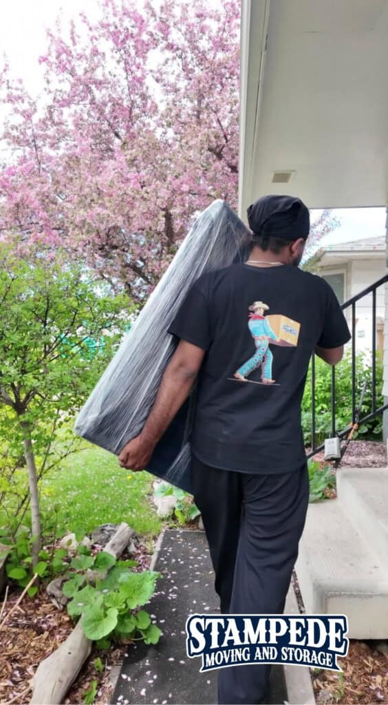 A Stampede Moving & Storage mover carefully carries protected furniture during a residential move in Calgary