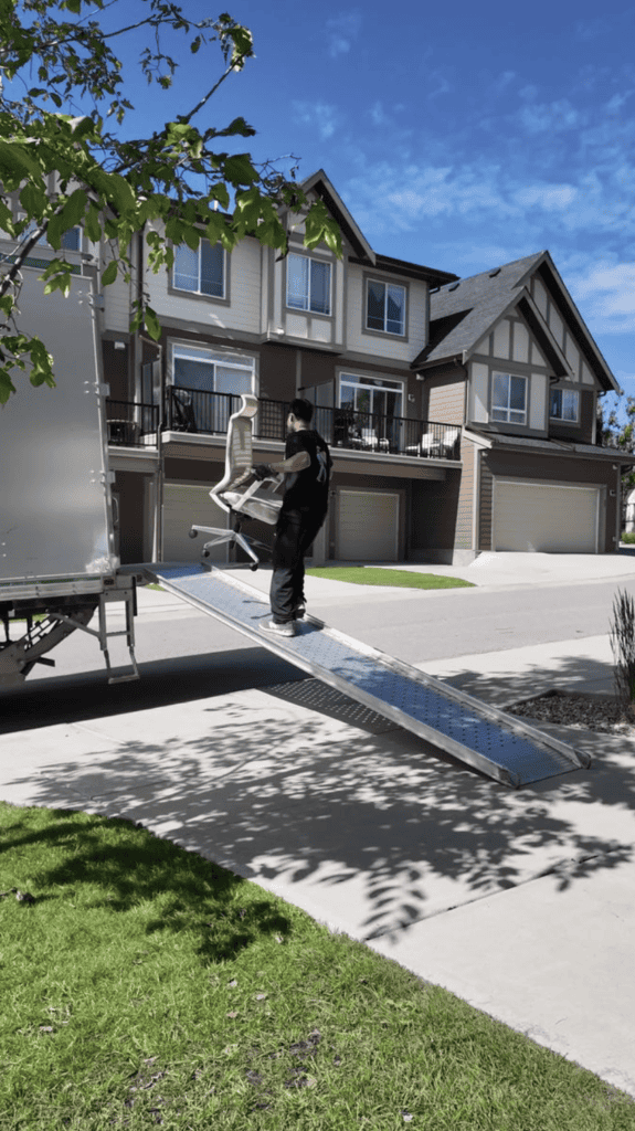 a professional mover carries an office chair up a moving truck ramp outside a residential townhouse, showcasing furniture loading during a home move